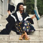 photo of woman wearing academic dress and floral dress sitting on stairway